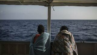 Dos migrantes hablan y observan el mar desde el Open Arms