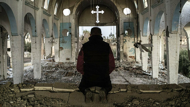 Un hombre reza en una iglesia siria destrozada