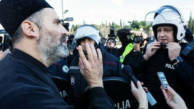 Un sacerdote de la Iglesia Ortodoxa Serbia habla con un policía antidisturbios en un puente cerca del parlamento, antes de votar el proyecto de ley sobre 'Libertades religiosas y derechos legales de las organizaciones religiosas' en Podgorica