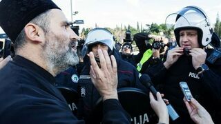 Un sacerdote de la Iglesia Ortodoxa Serbia habla con un policía antidisturbios