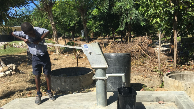 Un niño extrae agua de un pequeño pozo de agua limpia en Jérémie, Haití
