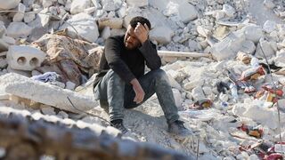 Un hombre sentado en los escombros en la zona afectada de Siria
