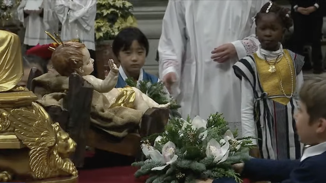 Un grupo de niños ponen flores al niño Dios