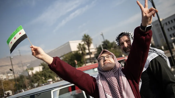 Una mujer, con la nueva bandera de Siria, celebra la caída de Al Asad
