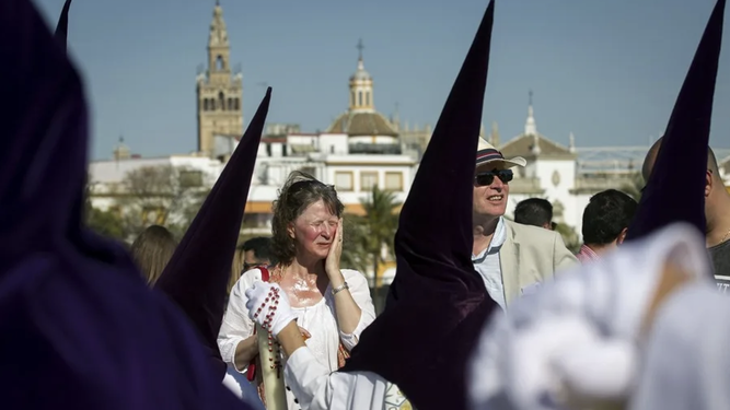 Unos turistas contemplan el paso de los nazarenos en Sevilla