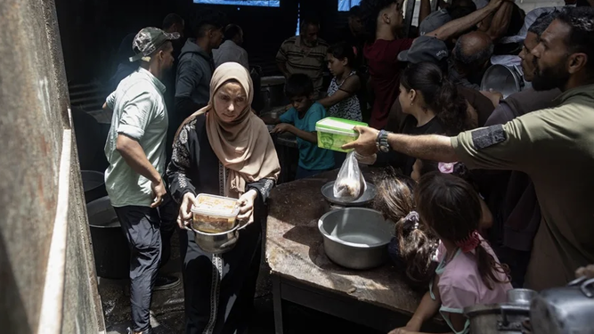 Una mujer recibe algo de comida en un comedor social en Gaza