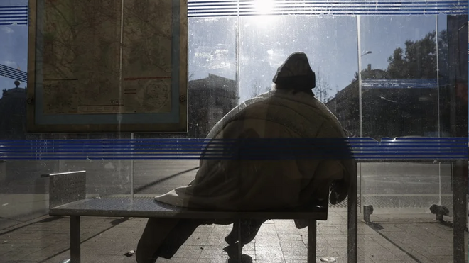 Un sintecho se cobija en una parada de autobús en Madrid